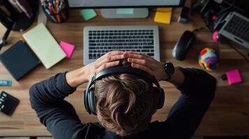 Frustrated person with headphones at cluttered desk, overwhelmed by work photo