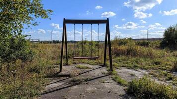 Abandoned swing set in overgrown field under blue sky and clouds photo