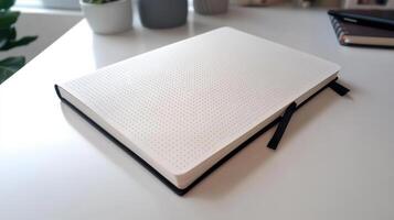A white notebook sitting on a desk next to a plant photo