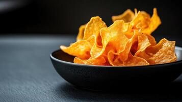Crispy golden taro chips in black bowl on dark surface photo