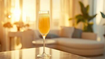 A refreshing Mimosa cocktail in a champagne flute, set on a marble countertop in a modern living room filled with warm natural sunlight. photo