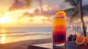 A Tequila Sunrise cocktail with bright layers of color, garnished with an orange slice, served in a tall glass by the ocean at sunset. photo