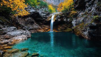 Serene Waterfall Cascading into a Crystal Clear Pool Surrounded by Autumnal Foliage and Rocky Cliffs photo