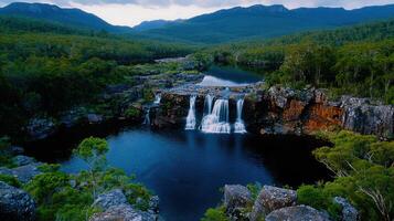 Serene Waterfall Cascading into a Deep Blue Pool Surrounded by Lush Green Foliage and Mountains photo