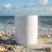 A white mug sits on a sandy beach, with waves and clouds in the background. photo