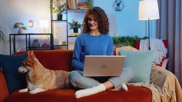 Woman freelancer using laptop netbook working on online project at home on sofa beside corgi dog video