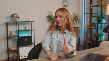 Happy Caucasian woman looking approvingly at camera showing thumbs up sitting at home office table video