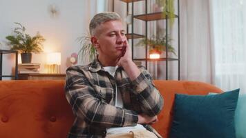 Thoughtful man sitting at home looks pensive thinks of unrequited love depressed bad feeling burnout video