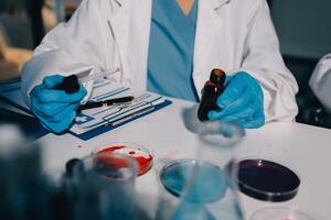 A person in a lab coat and gloves holding a vial photo