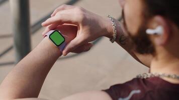 Athletic man looking at left hand with smartwatch chroma key, touching interacts with green screen video