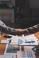 Business people shaking hands over a table with papers and graphs photo