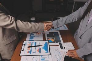 Two business people shaking hands over a table with papers and graphs photo
