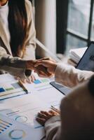 Business people shaking hands over a table with graphs and papers photo