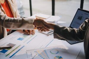 Two business people shaking hands over a table with graphs and papers photo