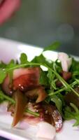 add cheese pieces to salad Chef of restaurant utilizes tongs in order to add slices of delectable, firm, and expensive cheese to vegetable salad garnished with bacon. Close up video