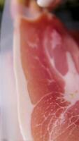 Thin slices of dry-cured prosciutto in close-up, process of delicacy slicing for antipasto plate preparation. High quality 4k footage video