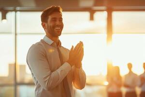 A smiling Caucasian man in a button-up shirt passionately applauding in a bright seminar room during sunset. photo