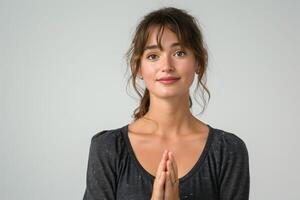 A young woman of Caucasian descent smiling softly with her hands in a prayer position, exuding a serene and welcoming vibe. photo