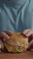 Client in blue T-shirt takes homemade burger with chicken cutlet and vegetables, with sauce flowing out of it, holding it in front of him, vertical video