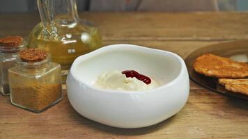 On wooden kitchen table of simple, rustic restaurant, stream of fresh ketchup is poured into deep bowl of mayonnaise and mixed with it. Recipe for burger sauce with chicken patty video