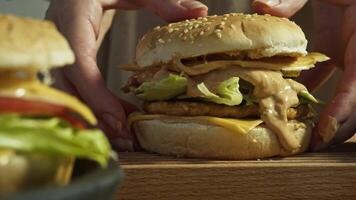 Chef prepares delicious burger by placing sesame bun on top and pressing it so that delicious sauce made from mayonnaise and ketchup flows out of hamburger. Close up. video