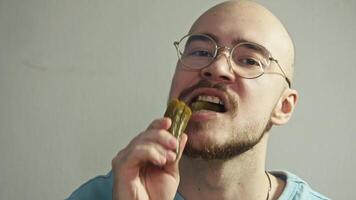 A bald man with glasses takes a bite of a pickled cucumber with a crunch and winces when he feels its sour-salty taste. Portrait. video