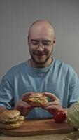 Man picks up homemade burger, following traditional American recipe, anticipating taste. He bites into it and enjoys bright, incredible flavor. Vertical. video