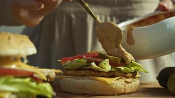 Cook pours generous amount of sauce onto burger, based on mayonnaise and ketchup. This gives burger delicious, juicy taste, but it also has high calorie content, making it fatty junk food. Close up. video