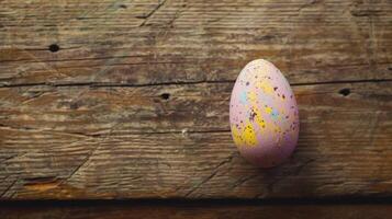 A single colorful speckled Easter egg rests on a rustic wooden surface photo