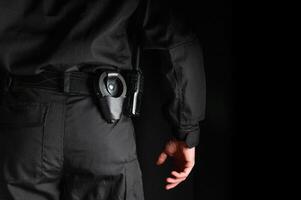 security guard controlling the premises. bodyguard in black uniform on black background, with handcuffs on his belt photo