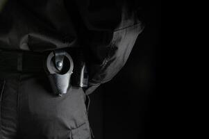 security guard controlling the premises. bodyguard in black uniform on black background, with handcuffs on his belt photo