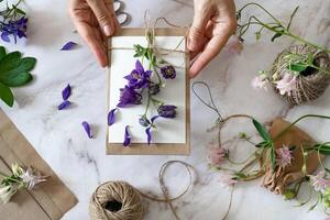 Closeup of hands of young woman florist creating invitation On a sunny day, put in envelope blossom flowers, top view. Macro. Isolated on white background. With free space for your text photo