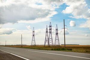 High voltage power lines leading through a green field. Transmission of electricity by means of supports through agricultural areas. photo