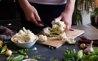 A woman cuts fresh cauliflower at the table On a sunny day photo