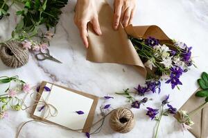 Closeup of hands of young woman florist creating invitation On a sunny, beautiful day put in envelope blossom flowers, top view. Macro. Isolated on white background. With free space for your text photo