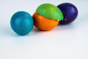 Three colorful dyed easter eggs in teal blue, orange purple, with cracked green shell. Isolated on white background. Playful colors. textures of holiday decorations. Copy space. Selective focus 12 photo