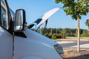 White camper van on a highway rest area with an open hood parked on a roadside for an engine check, indicating trouble or maintenance during a road trip. Copy space 1 photo