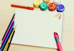 Creative workspace with blank paper, colorful markers, and paint on a wooden table photo