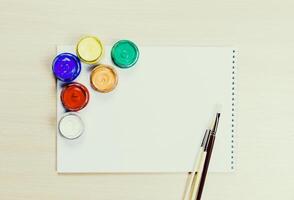 Colorful paints and brushes arranged on a blank sketchpad ready for creative expression photo