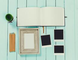 Creative workspace with blank notebook, picture frame, and instant photos on a turquoise wooden table