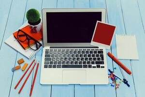 Workspace setup with laptop, stationery, and creative elements on a blue wooden table photo