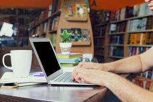 Focused individual working on laptop in a cozy library setting with coffee and books photo