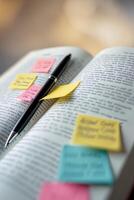 Collection of colorful sticky notes on an open book with a black pen ready for note-taking during study session photo
