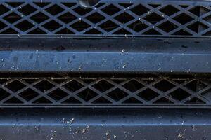 Closeup of a dirty bug splattered vehicle grille with dust and debris. Car front end bumper covered in insects and dirt after a long trip. Auto care, road conditions, air intake system photo