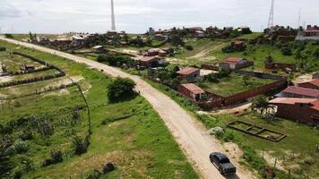 Aerial drone image of a car passing by some houses and wind turbines in the background video