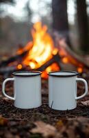 Two white enamel mugs by campfire on ground photo