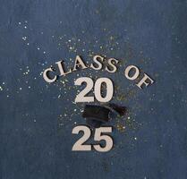 Graduation cap on wooden number 2025 on dark background. Class of 2025 photo