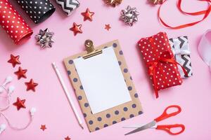 Blank sheet of paper and christmas presents with wrapping paper flat lay on pink background photo