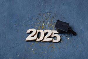 Graduated cap on wooden number 2025 on dark background. Class of 2025 concept photo