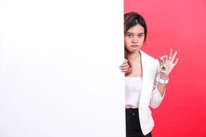 A woman partially visible behind a white board is holding keys with a house symbol on them, isolated on a red background. photo